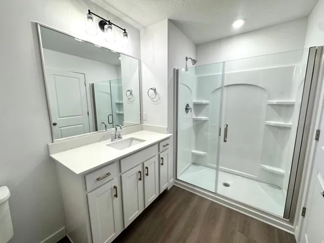 Contemporary bathroom featuring a white vanity with an integrated sink, a large framed mirror, and a sleek glass-enclosed shower with built-in shelving