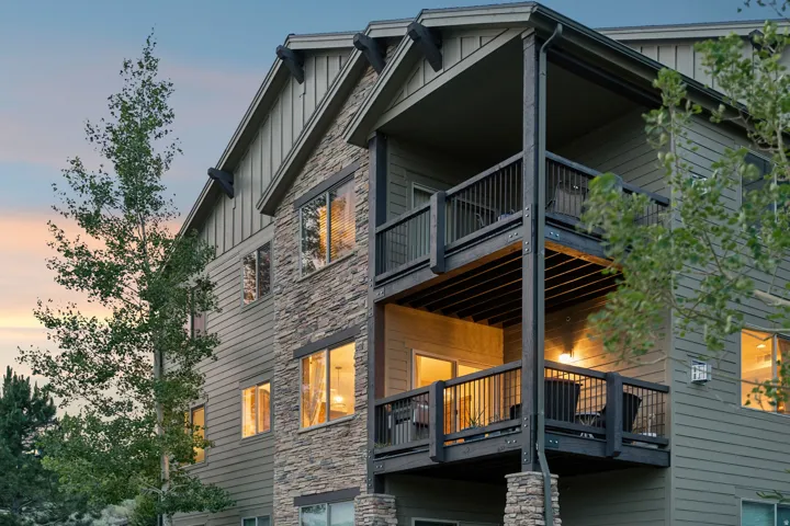 Modern two-story residence featuring mixed exterior materials including stone and horizontal siding, multi-level composite decking with metal railings, and expansive glazing throughout