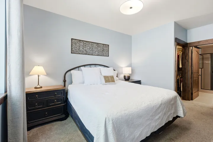 Serene primary bedroom featuring a queen-size bed with metal headboard, soft white bedding, and coordinating throw pillows