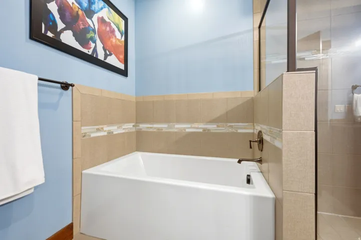 Modern bathroom featuring a soaking tub with chrome fixtures, ceramic tile surround with decorative accent band, frameless glass shower enclosure, wall-mounted towel bar, and soft blue accent wall paired with neutral tile finishes