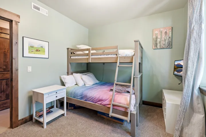 Spacious bedroom featuring a wooden bunk bed with built-in storage, carpet flooring, and soft natural lighting