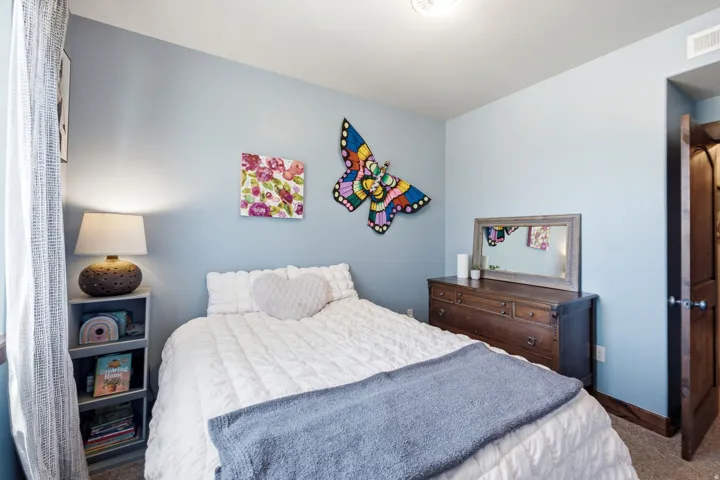 Comfortable secondary bedroom featuring soft blue walls, wood-finish flooring, and a wood dresser with mirror