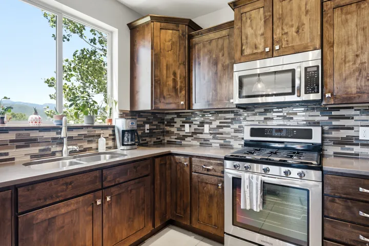 Chef's kitchen featuring rich wood cabinetry, stainless steel appliances including a gas range and built-in microwave, mosaic tile backsplash, and light-filled countertops