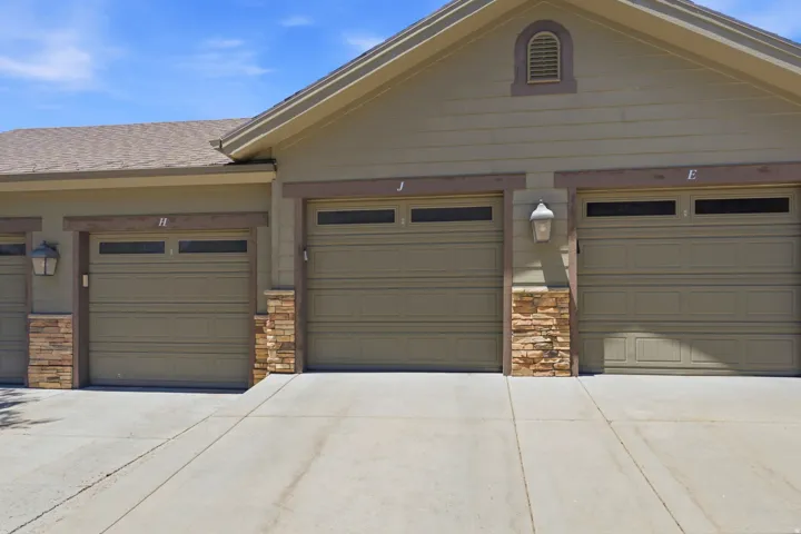 Three-car garage featuring neutral-toned sectional doors with windows, stone pillar accents, and a wide concrete driveway