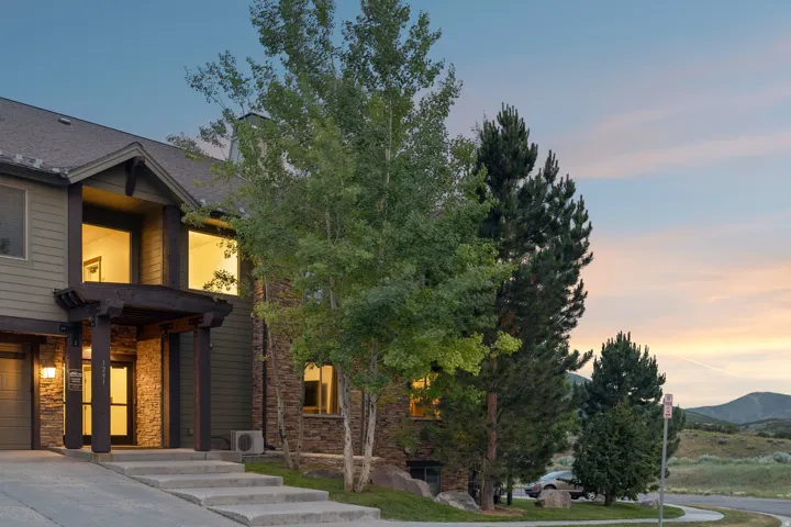 Modern architectural home featuring a striking two-story design with board-and-batten exterior siding, expansive glazing with black-framed windows and glass doors, and warm interior lighting