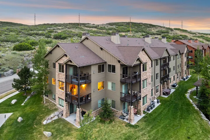 Modern multi-unit residential complex featuring stacked stone and composite siding exterior, multiple gabled rooflines with architectural detailing, and illuminated windows
