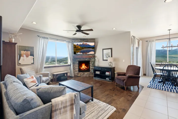Spacious great room anchored by a gas fireplace with stone surround, offering panoramic windows framing mountain scenery