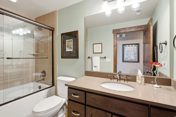 Spa-inspired master bathroom featuring a dual-sink vanity with wood cabinetry and quartz countertop, large framed mirror with integrated lighting, and a walk-in shower with glass enclosure and tile surround