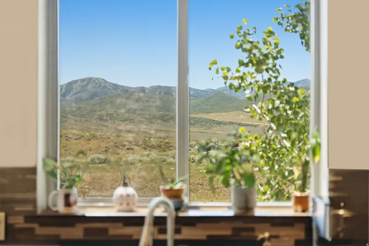 Expansive landscape featuring distant mountains and natural terrain, framed by a window with a wood-finish sill and a visible faucet