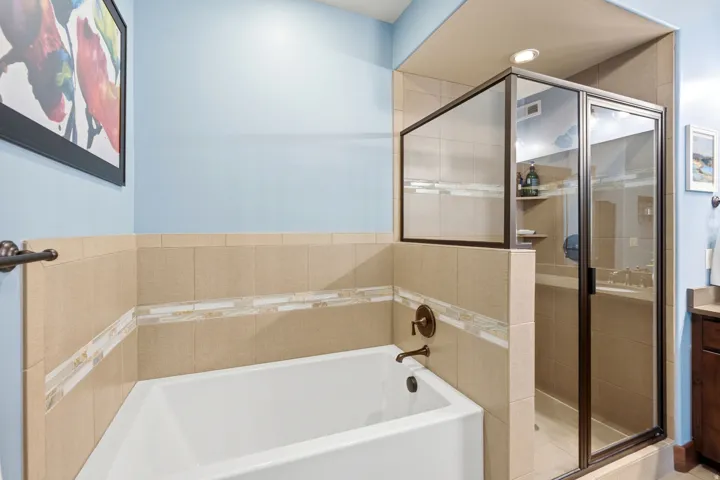 Primary Bathroom featuring a white soaking tub with chrome fixtures, frameless glass-enclosed shower with sliding doors and tile surround, and dual-zone layout