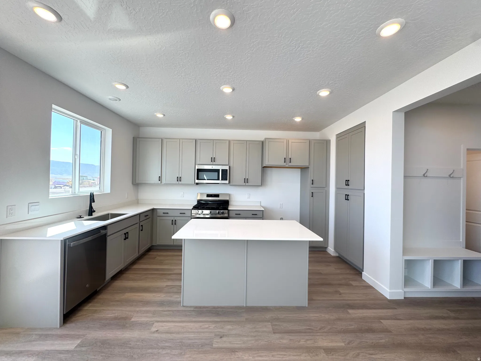 Kitchen featuring a central island, light gray cabinetry with black hardware, stainless steel appliances, and a double basin sink