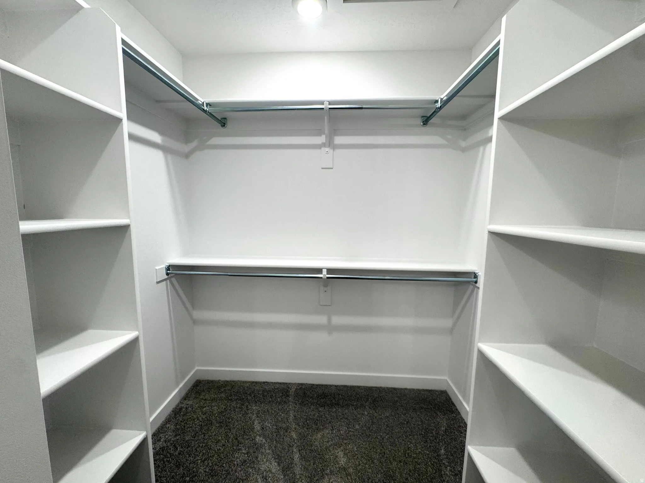 Walk-in closet featuring built-in shelving, chrome hanging rods, recessed lighting, and dark textured carpet