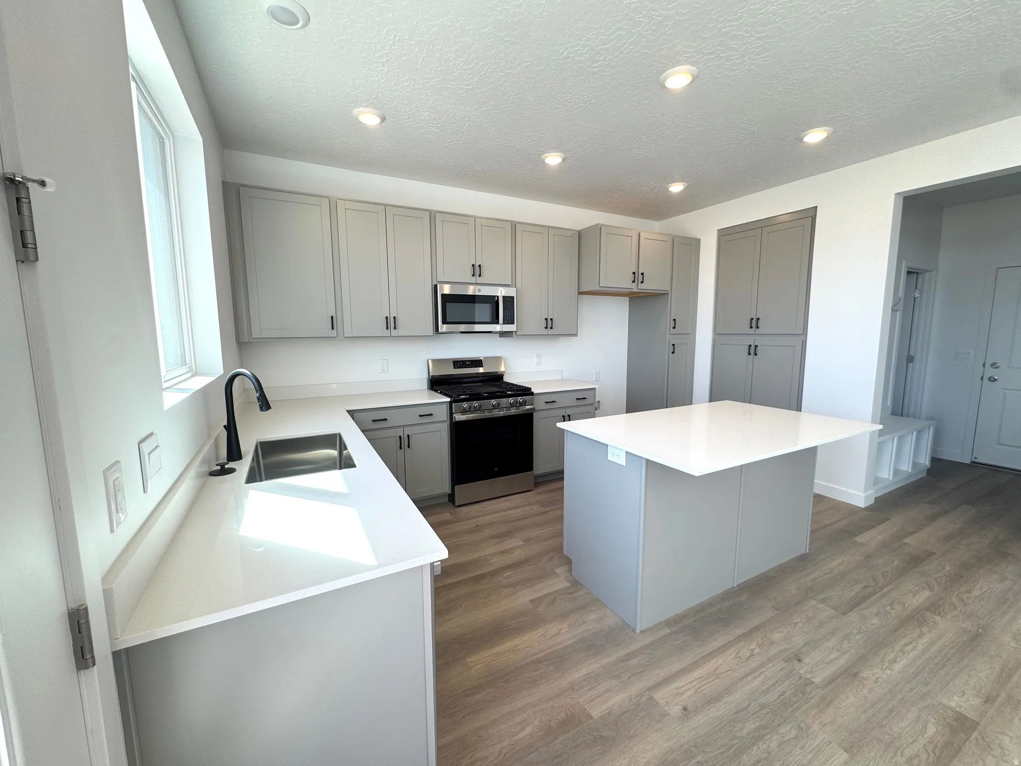 Modern kitchen featuring light gray cabinetry, stainless steel appliances, a center island with a white countertop, recessed lighting, and wood-finish flooring