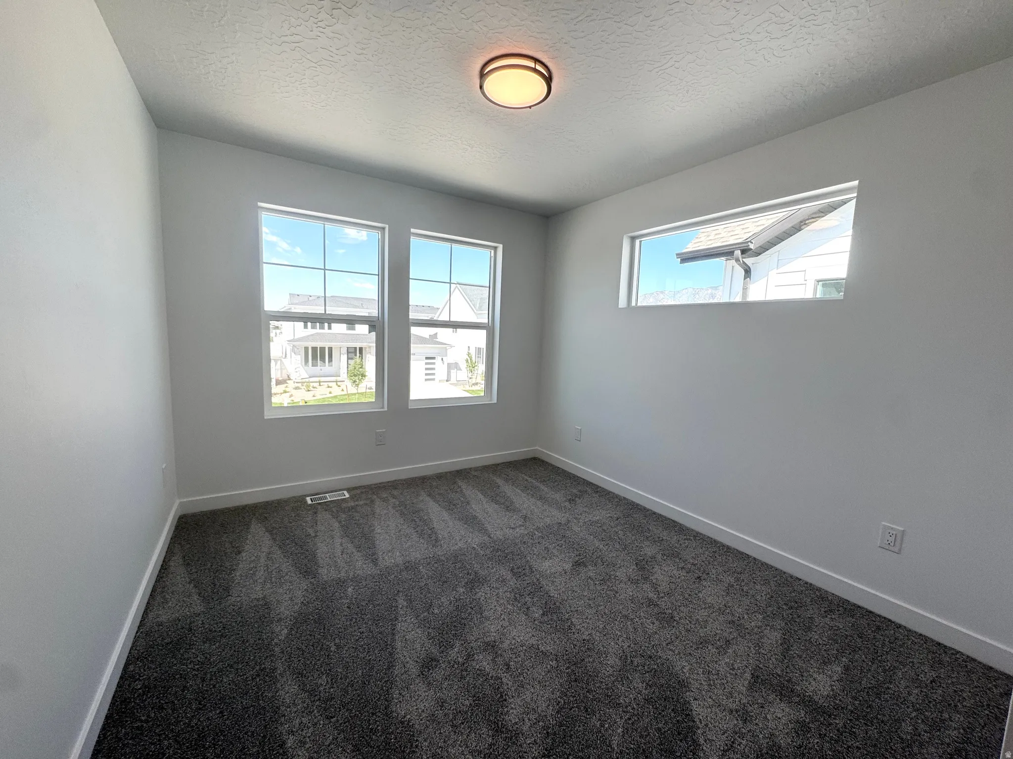 Room featuring neutral white walls, dark gray patterned carpeting, and white baseboards