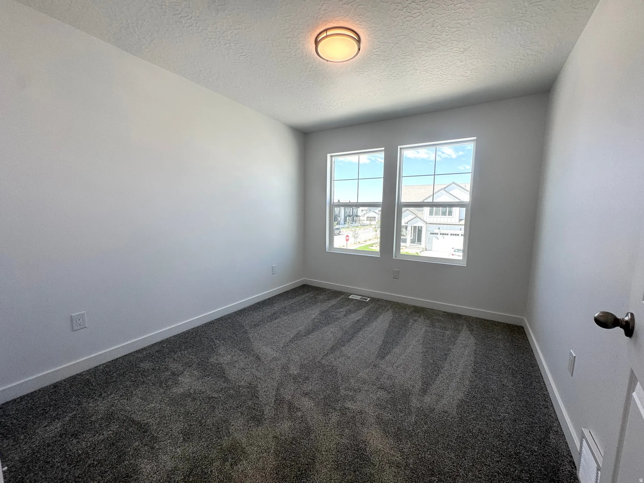 Bright room featuring dual windows, patterned carpet flooring, white baseboards, and a flush-mount ceiling light