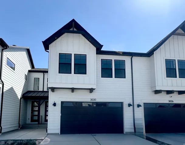 Modern farmhouse exterior with white board and batten siding, black trim windows, a dark garage door, and decorative exterior lighting