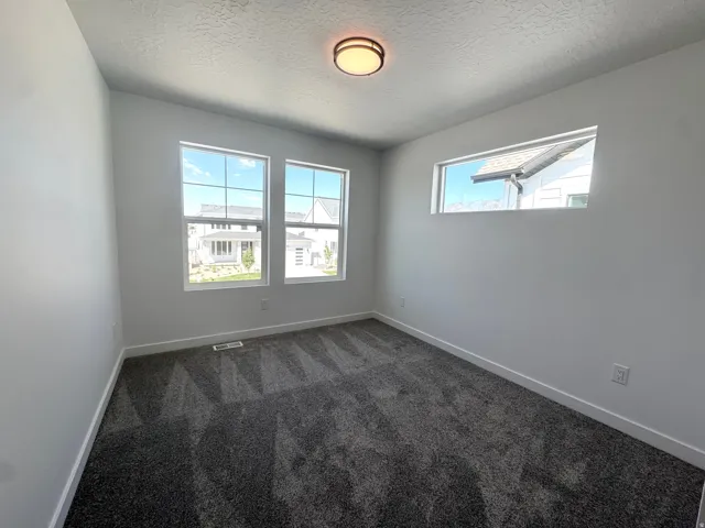 Room featuring neutral white walls, dark gray patterned carpeting, and white baseboards