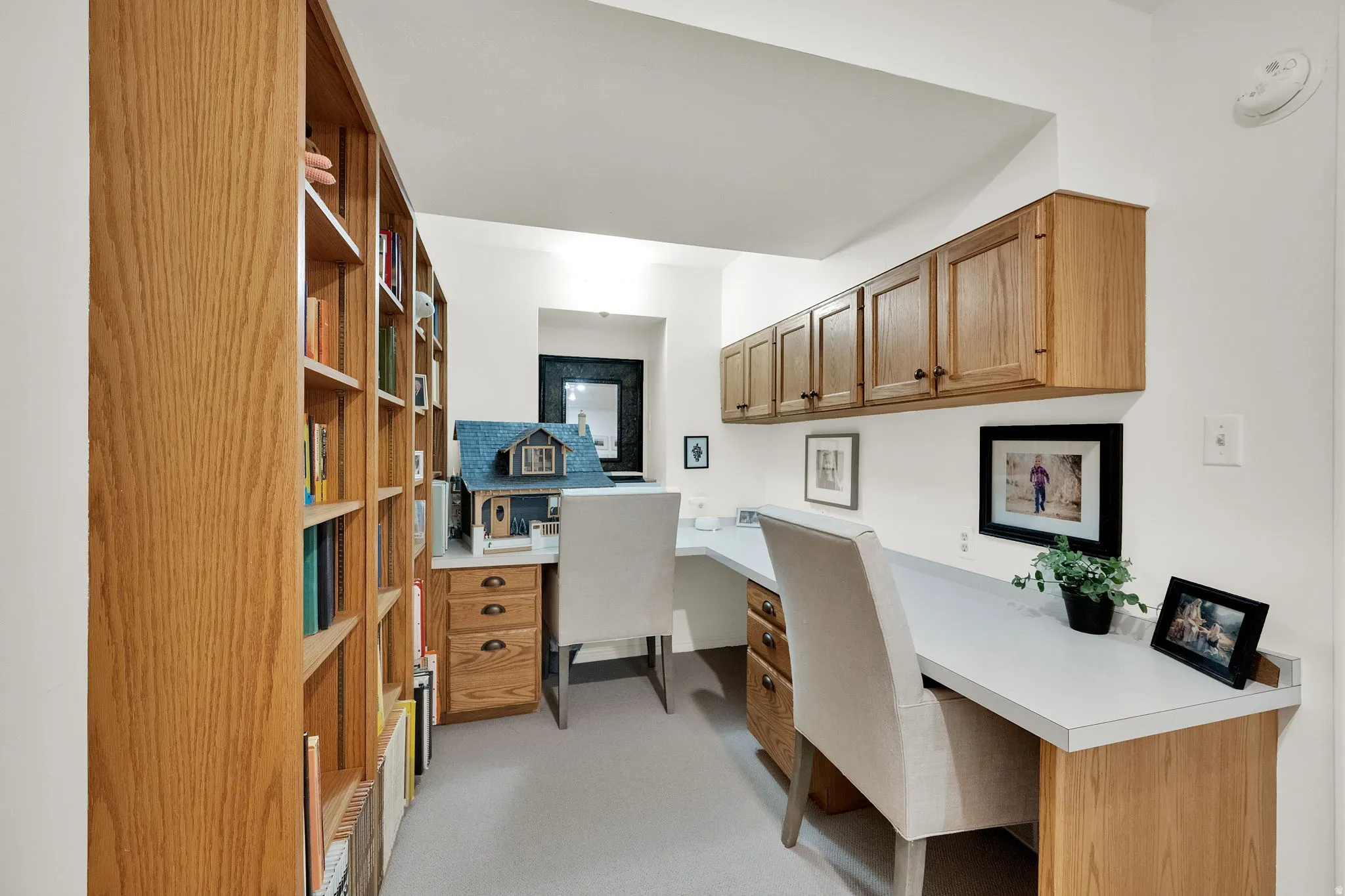 Dedicated office space featuring extensive built-in oak bookcases, integrated desks with wood-finish cabinetry, and overhead oak storage cabinets