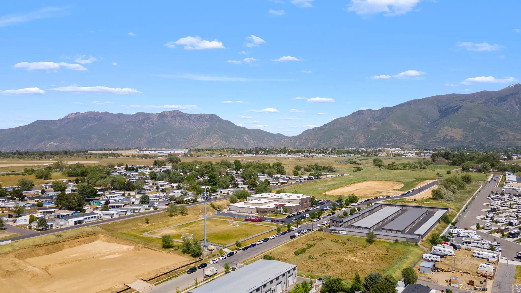 Expansive aerial perspective showcasing a mountainous backdrop, a mix of residential structures, and open land