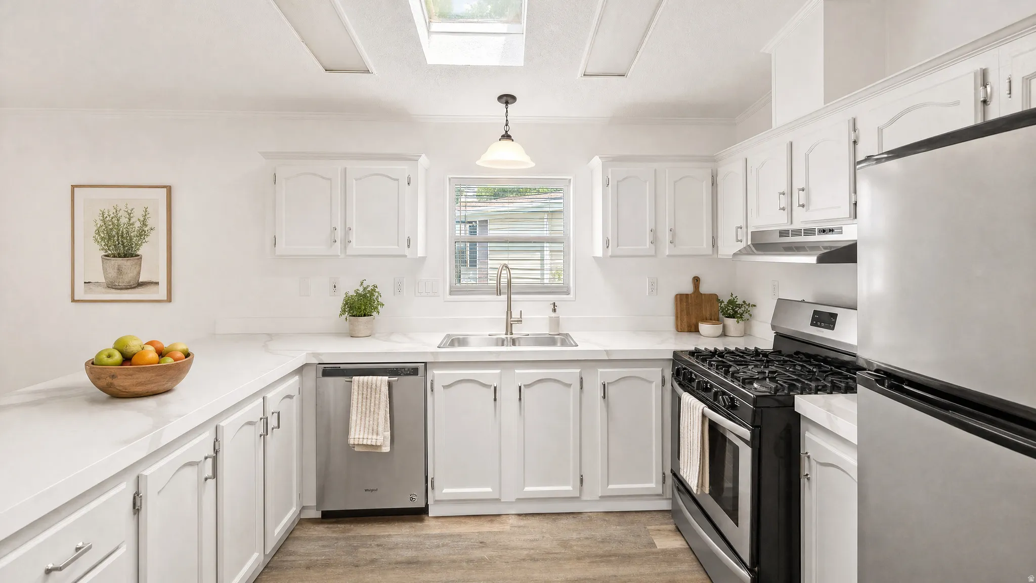 Bright kitchen featuring white cabinetry, light countertops, wood-finish flooring, a stainless steel gas range, and a skylight