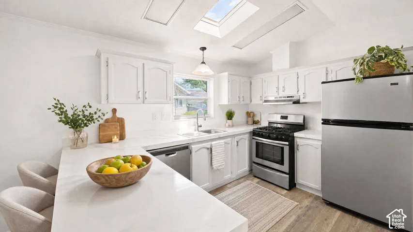 Kitchen featuring white cabinetry, light-colored countertops, wood-finish flooring, stainless steel appliances, and a skylight