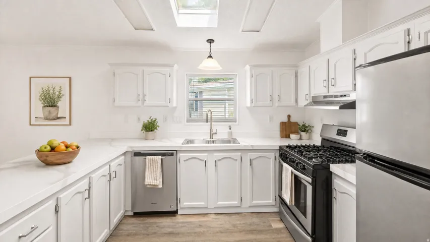 Bright kitchen featuring white cabinetry, light countertops, wood-finish flooring, a stainless steel gas range, and a skylight