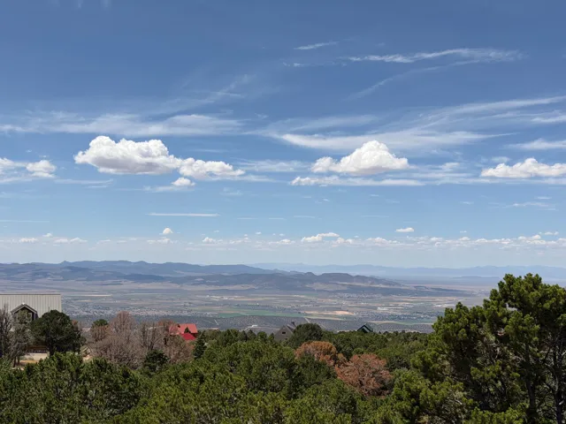 Expansive blue sky with scattered clouds above a distant mountain range and valley