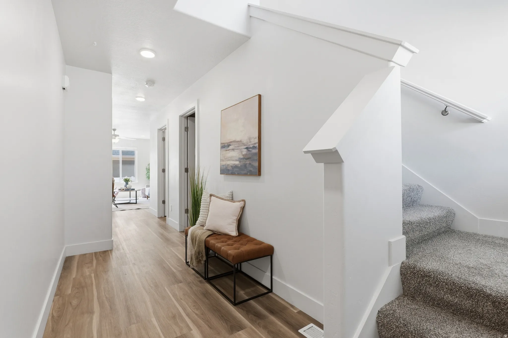 Bright interior hallway featuring wood-finish flooring, recessed lighting, white trim, and a carpeted staircase with a white handrail
