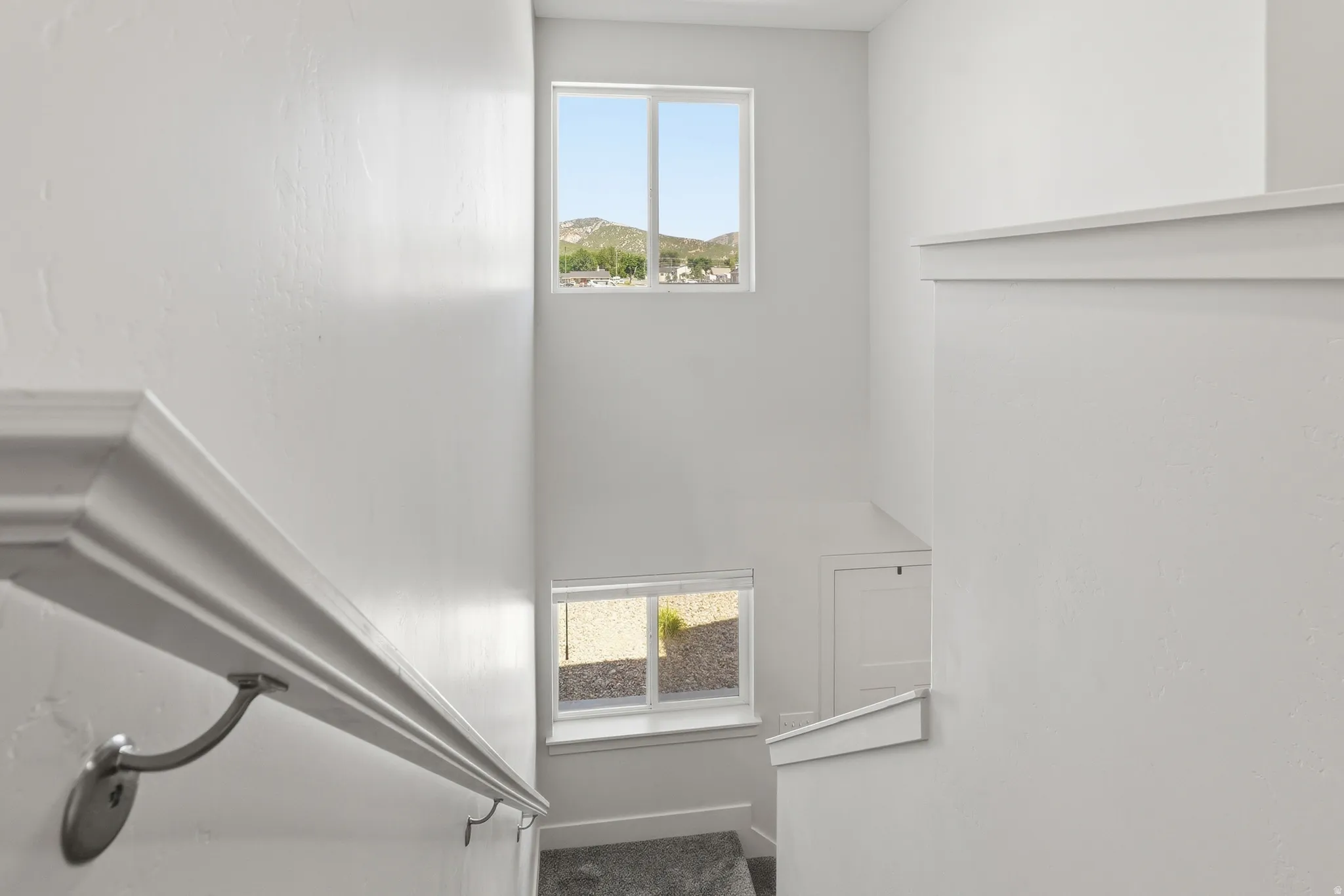 Stairwell with carpeted steps, white walls, and a white handrail with brushed nickel brackets