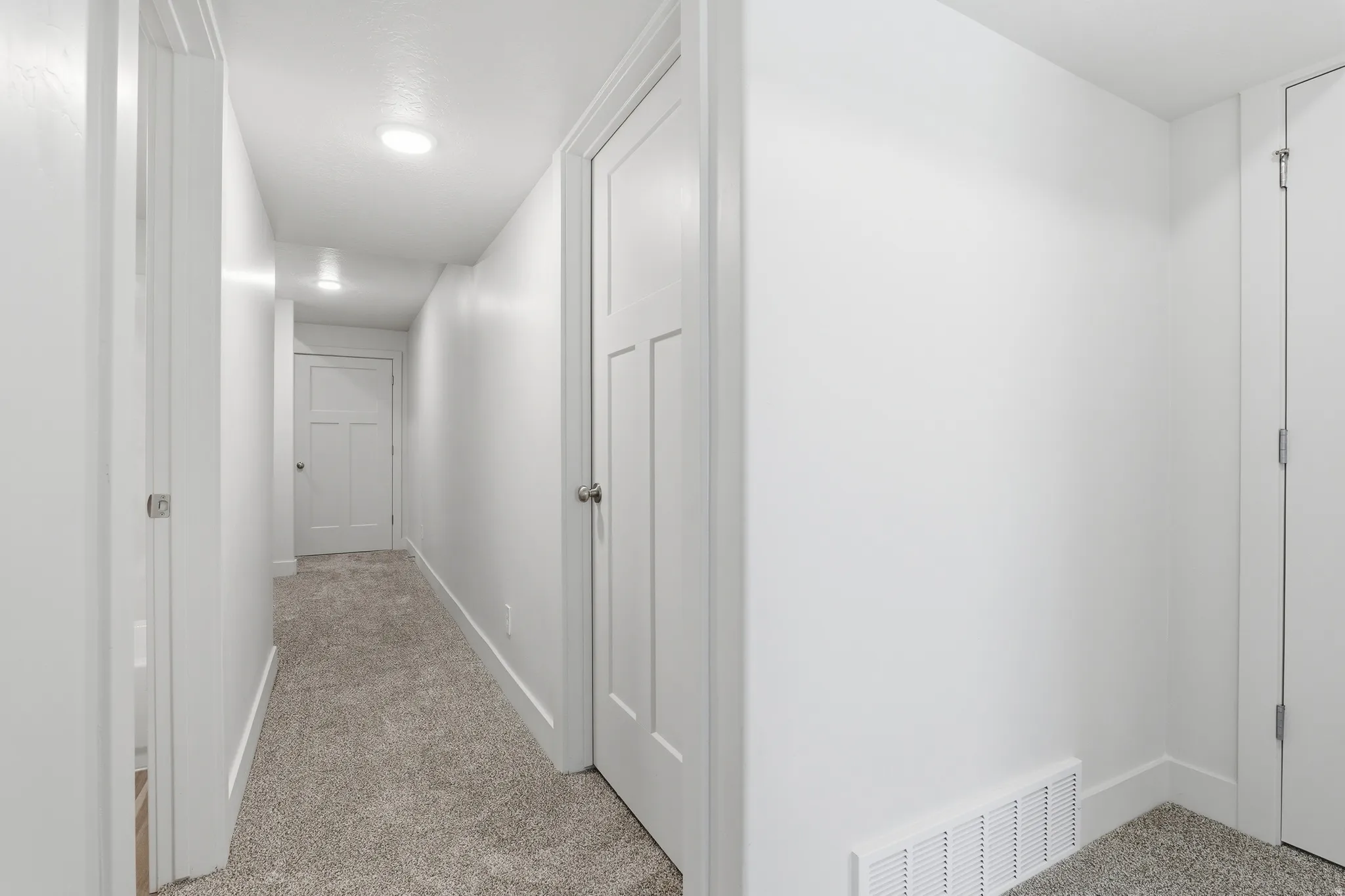 Hallway with neutral carpeting, recessed lighting, white panel doors, and crisp white trim