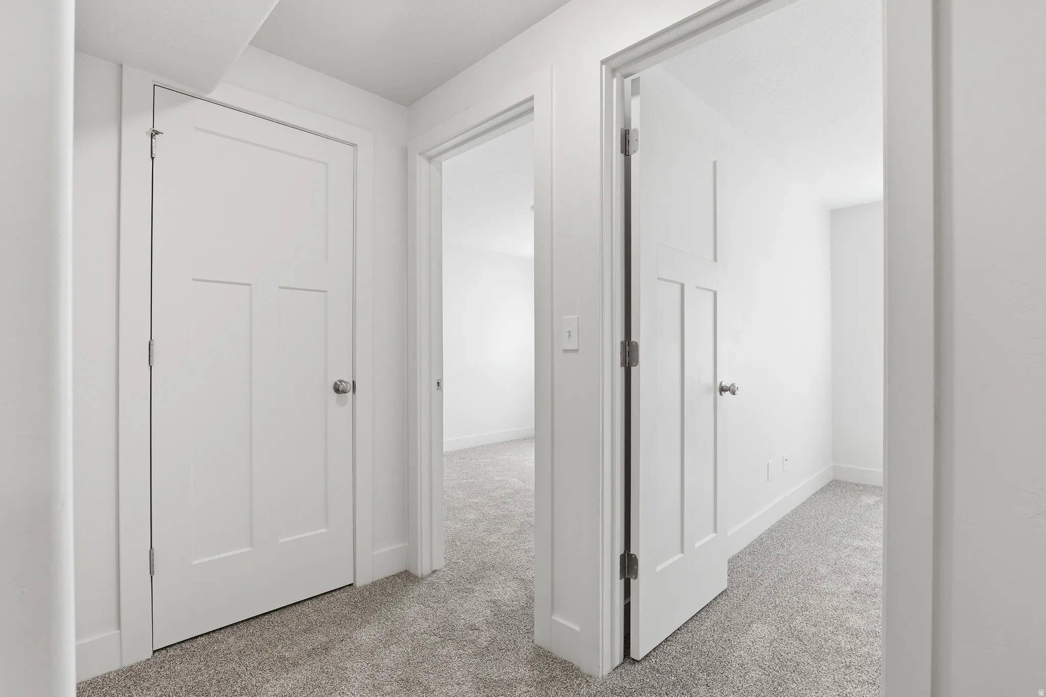 Hallway featuring crisp white walls and doors, light gray carpeting, and white trim
