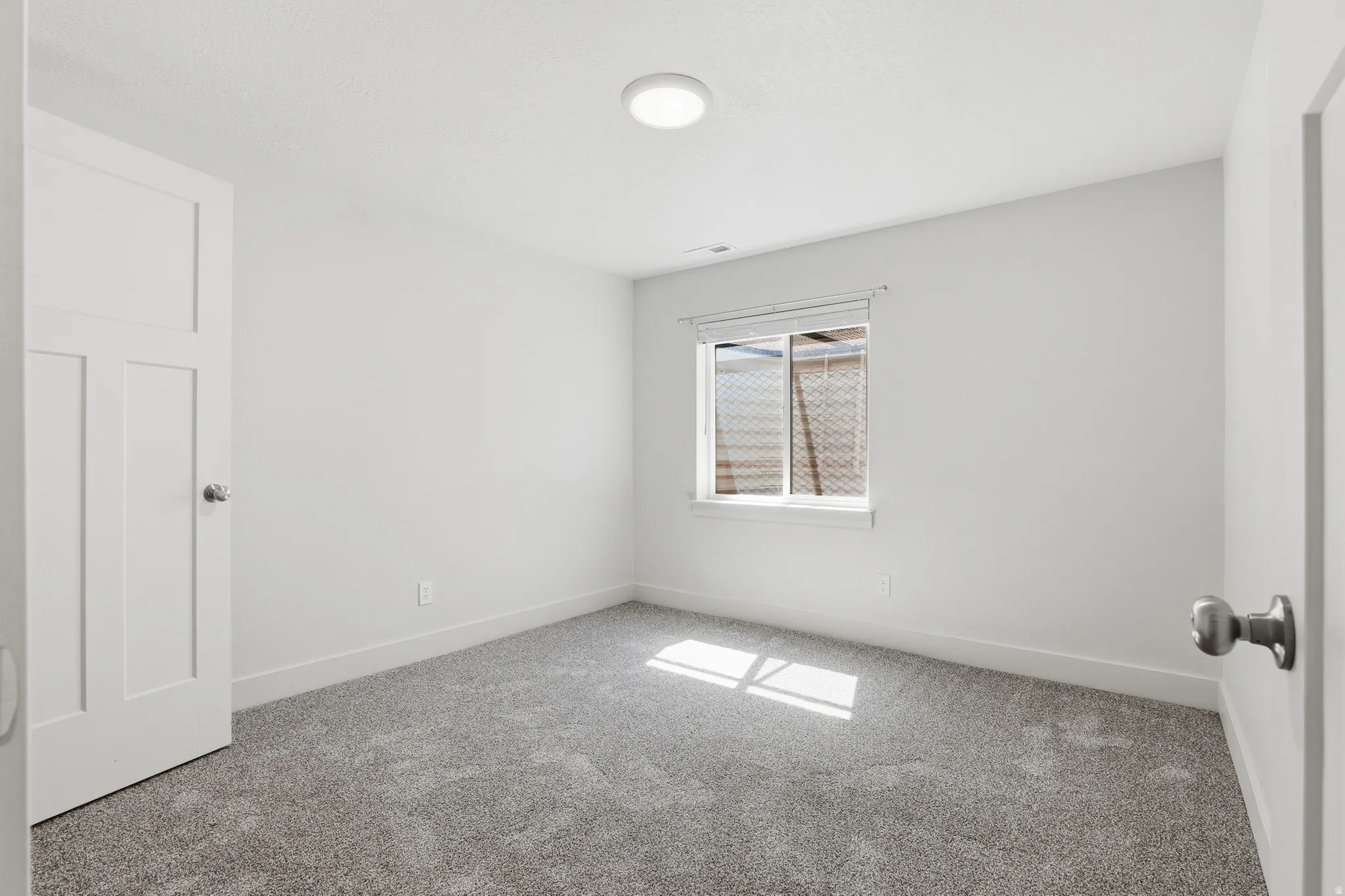 Bright room featuring neutral gray carpeting and a single window with blinds