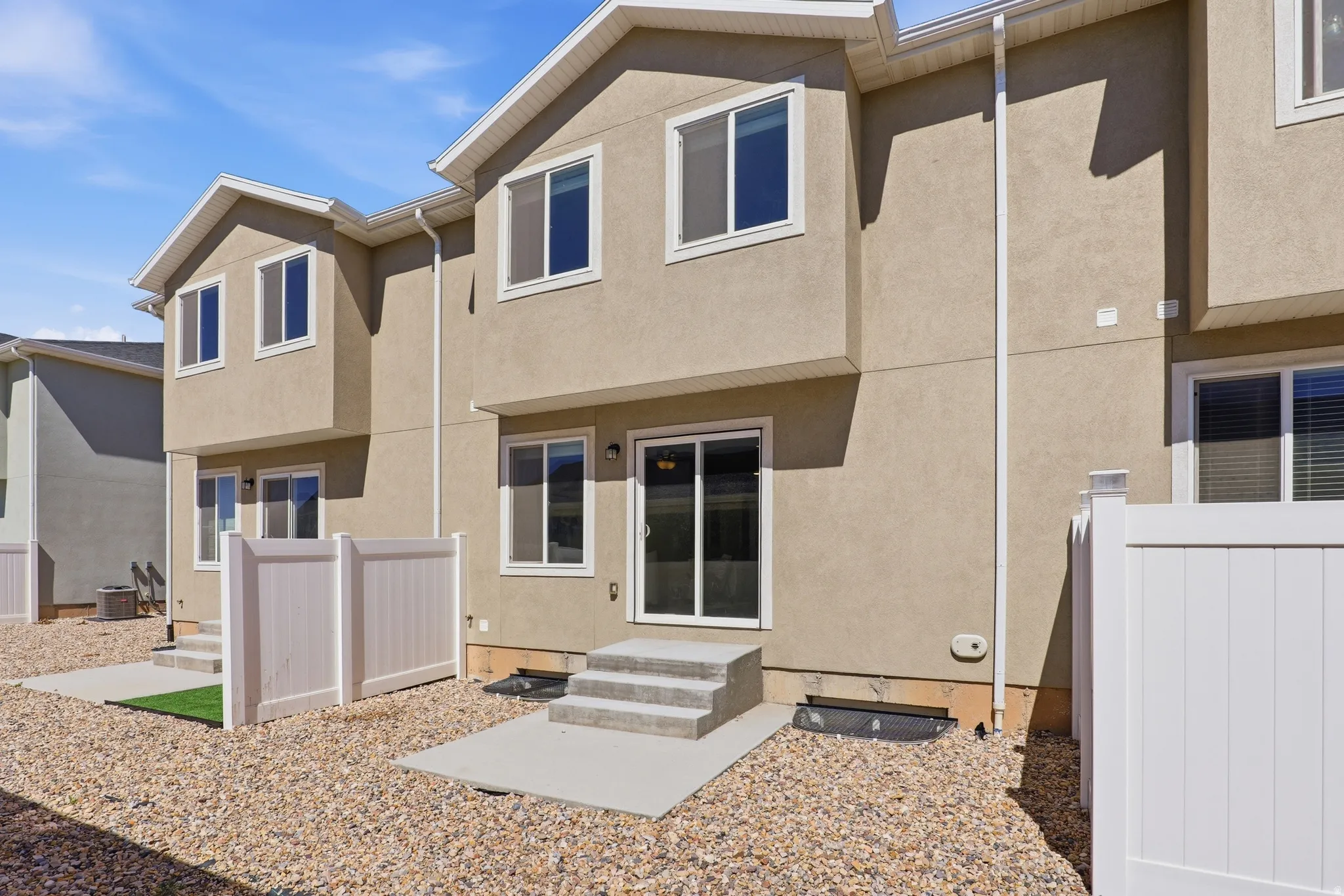 Rear exterior featuring stucco siding, white vinyl fencing, concrete patios, and gravel landscaping
