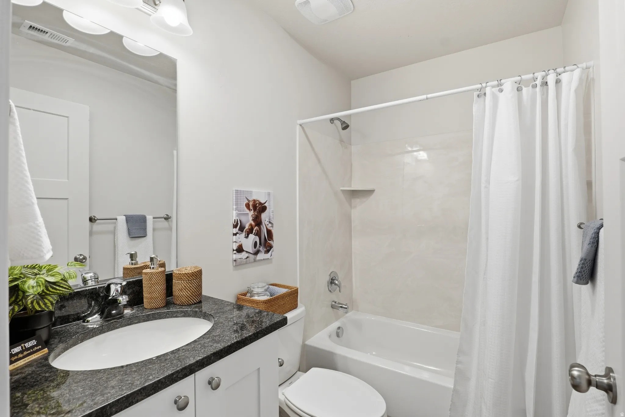 Bathroom featuring a vanity with a dark speckled countertop, an undermount sink, and white cabinetry