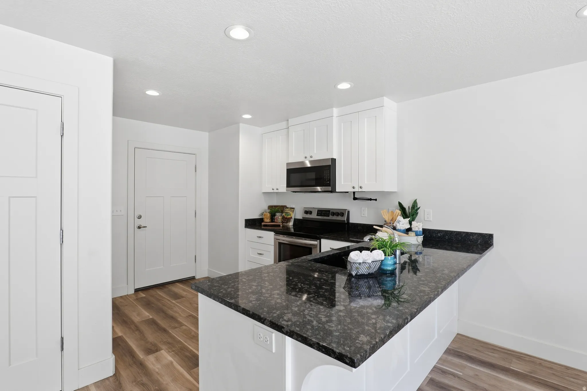 Kitchen featuring a dark granite countertop with an integrated sink, white cabinetry, stainless steel appliances, and wood-finish flooring