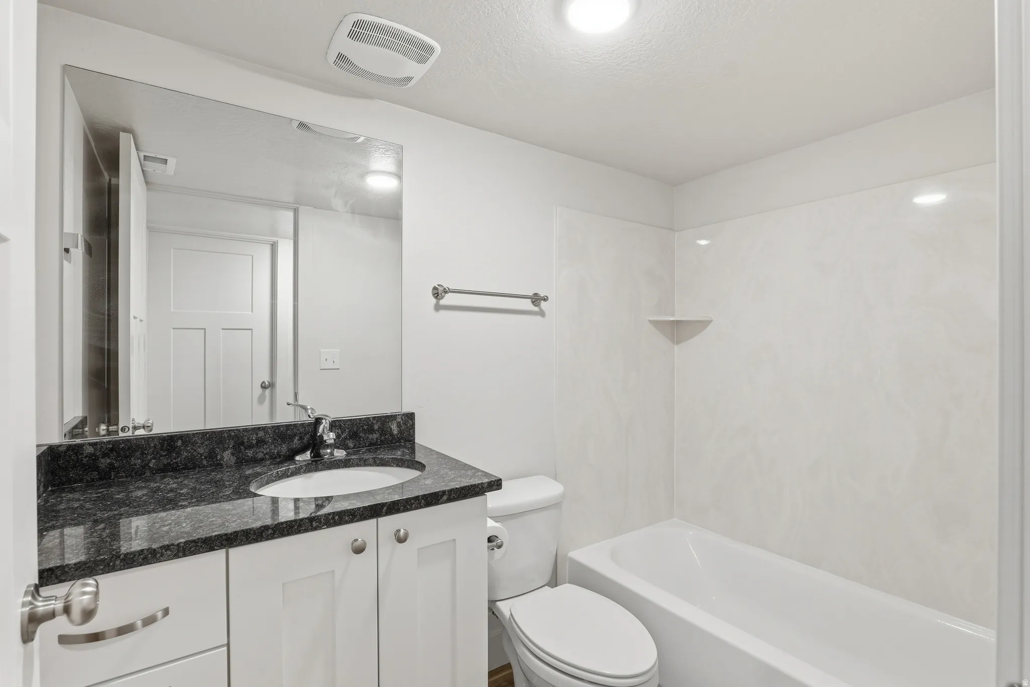 Bathroom featuring a white vanity with a dark speckled countertop, an undermount sink, and a large wall-mounted mirror