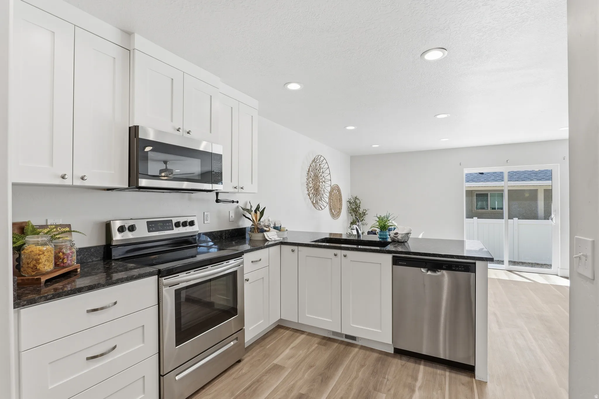 Modern kitchen featuring white shaker cabinetry, stainless steel appliances, dark countertops, recessed lighting, and wood-finish flooring