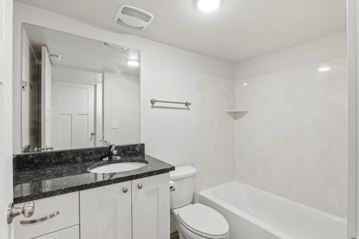 Bathroom featuring a white vanity with a dark speckled countertop, an undermount sink, and a large wall-mounted mirror