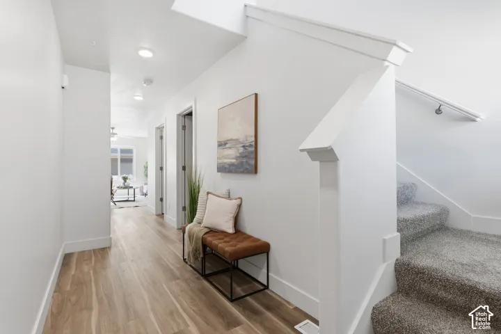 Bright interior hallway featuring wood-finish flooring, recessed lighting, white trim, and a carpeted staircase with a white handrail