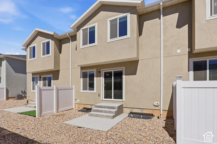 Rear exterior featuring stucco siding, white vinyl fencing, concrete patios, and gravel landscaping