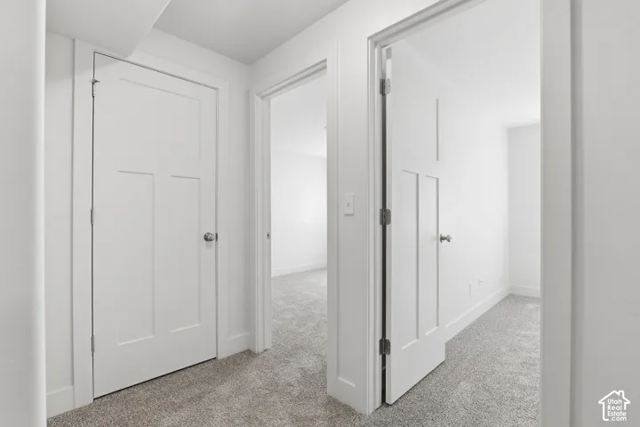Hallway featuring crisp white walls and doors, light gray carpeting, and white trim