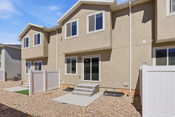 Rear exterior featuring stucco siding, white vinyl fencing, concrete patios, and gravel landscaping