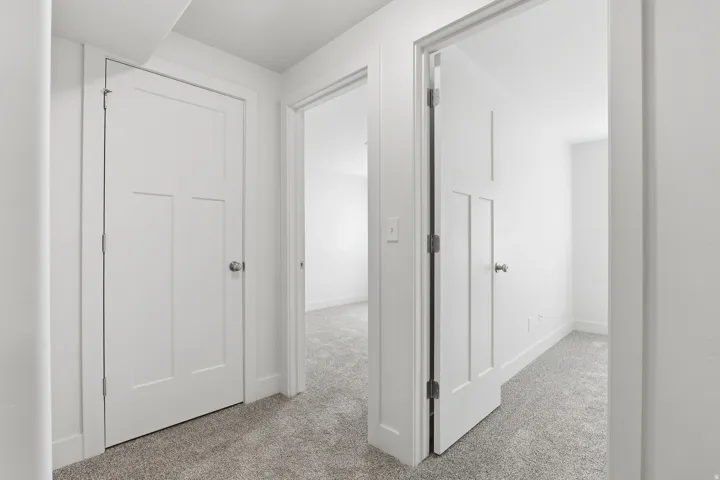 Hallway featuring crisp white walls and doors, light gray carpeting, and white trim