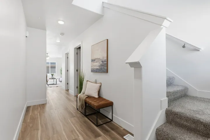 Bright interior hallway featuring wood-finish flooring, recessed lighting, white trim, and a carpeted staircase with a white handrail