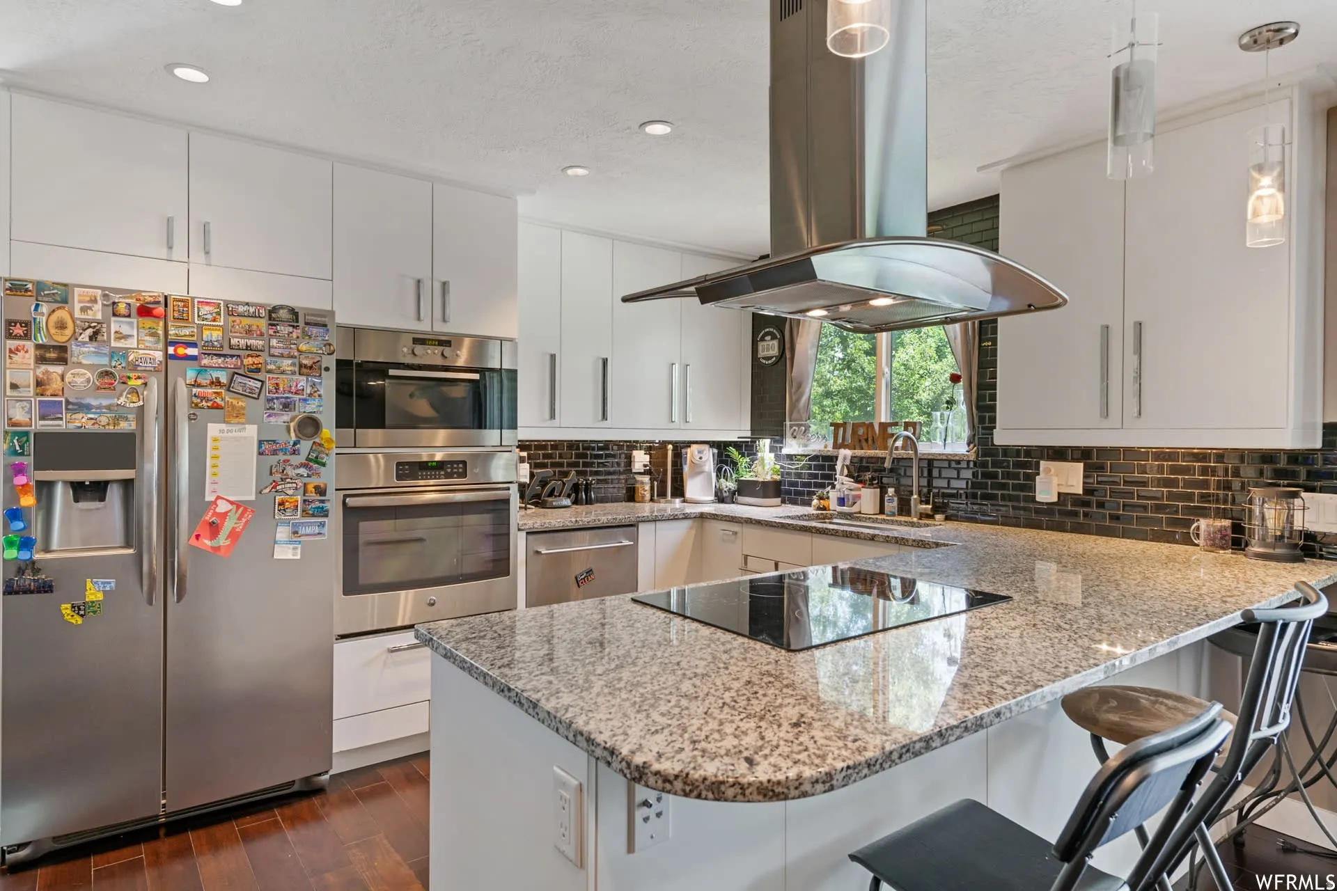Modern kitchen featuring white cabinetry, stainless steel appliances, a center island with a built-in cooktop, granite countertops, and a dark tile backsplash