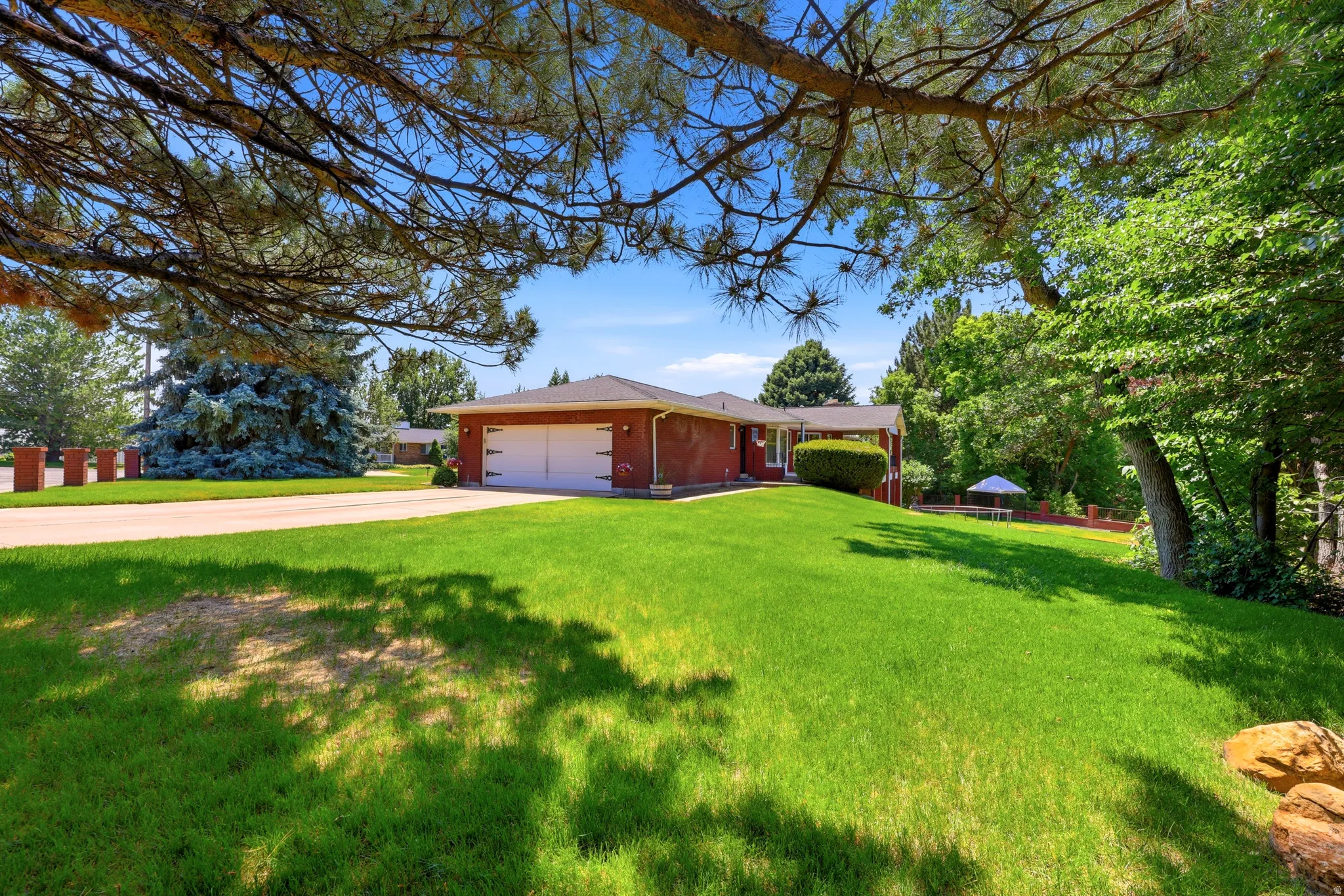 Expansive front yard featuring a manicured lawn, mature trees, and a brick exterior home with an attached garage