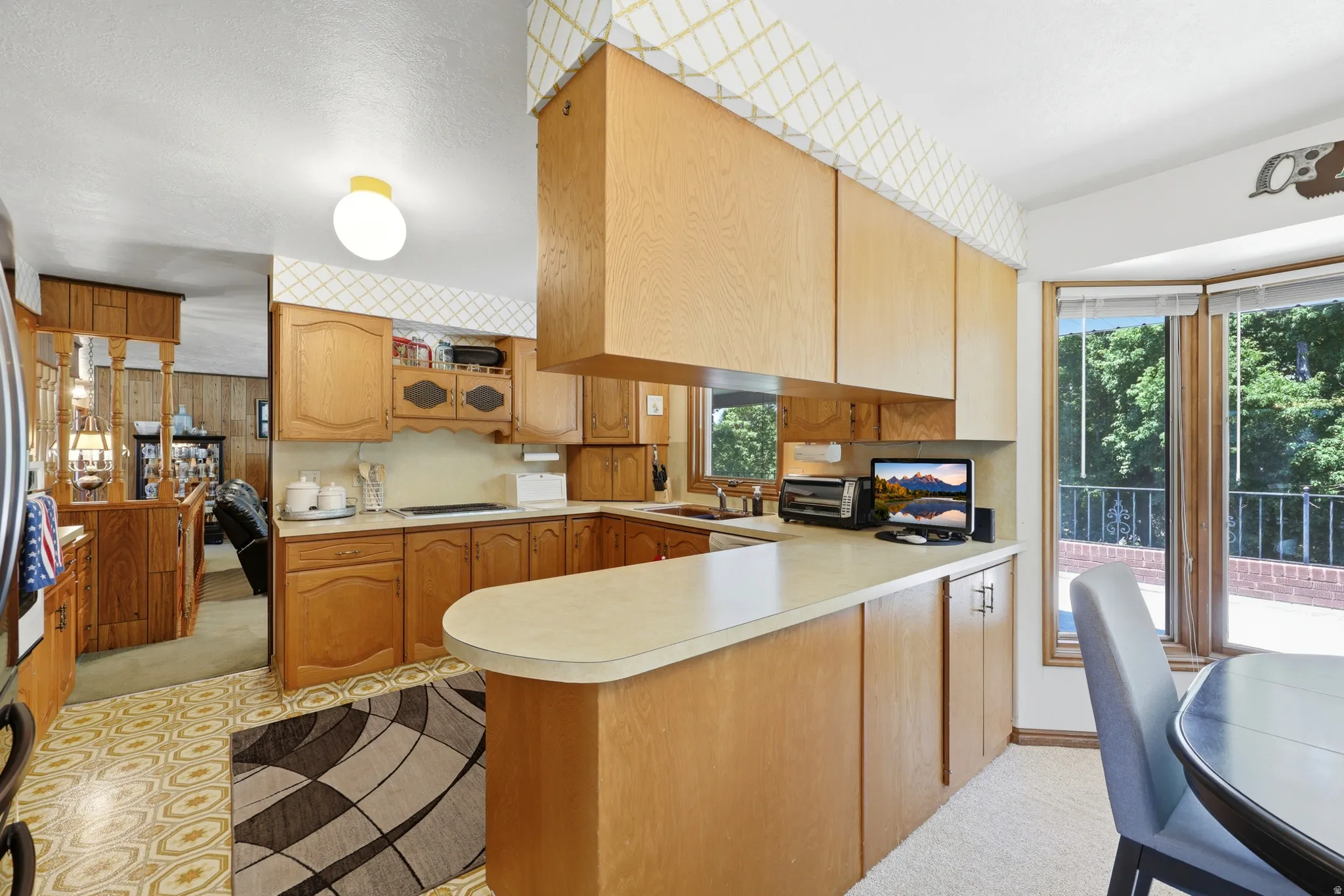 Kitchen featuring light wood cabinetry, a peninsula counter with a rounded edge, patterned floor tile, and a bay window with a surrounding outdoor brick patio