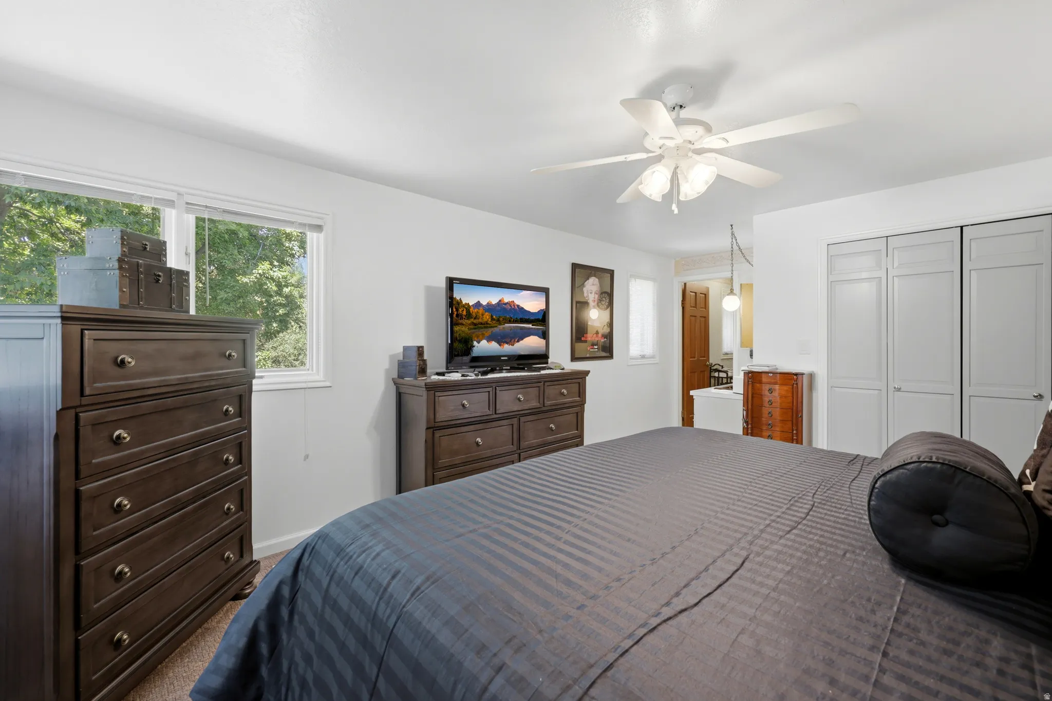 Bright interior with natural light, featuring a ceiling fan with integrated lighting, wood-finish flooring, and built-in closet doors