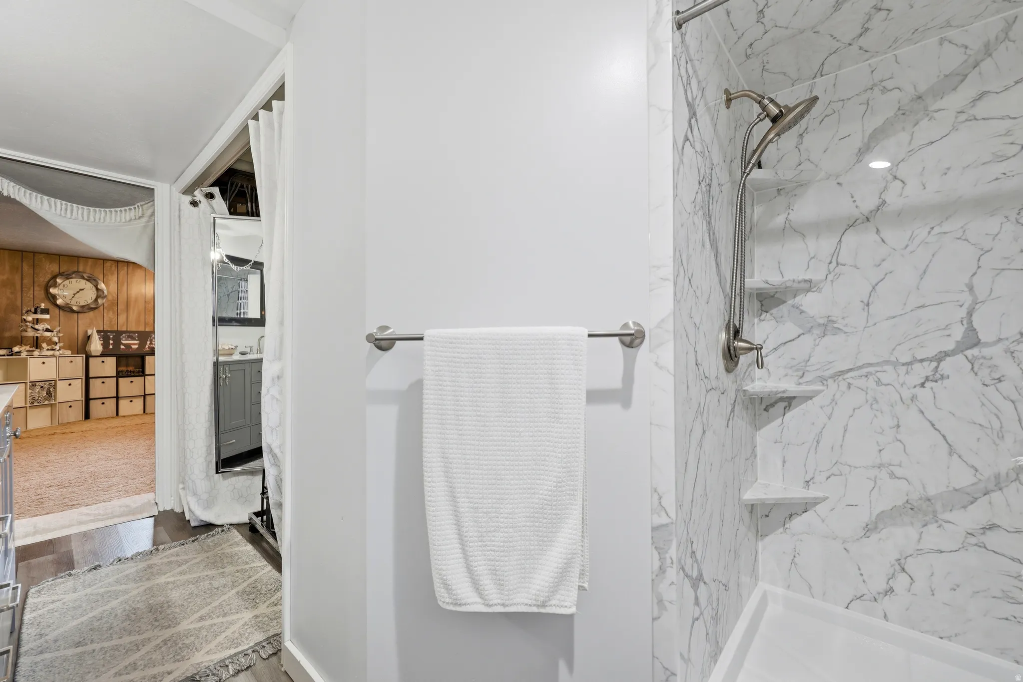 Shower featuring white marble-patterned paneling, built-in corner shelving, and a brushed nickel shower fixture
