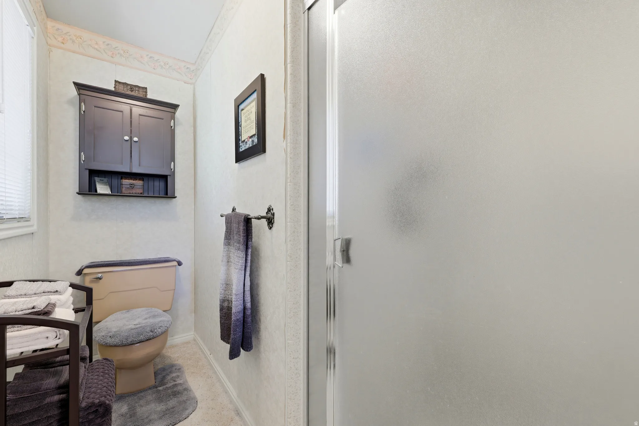 Bathroom featuring a frosted glass shower enclosure, wall-mounted storage cabinet, and window with blinds